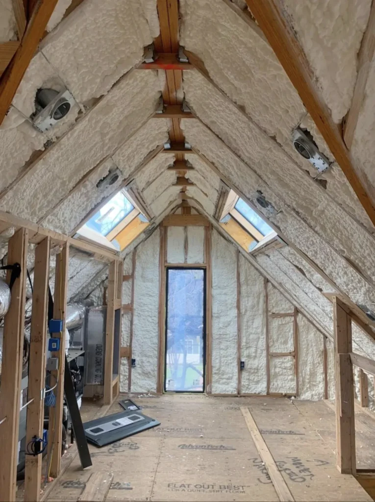Attic insulated with spray foam on the roof rafters and gable wall, with two skylights and a tall window