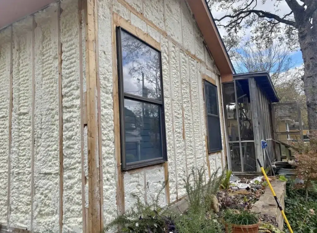 Exterior house wall with spray foam insulation between wood studs around the windows