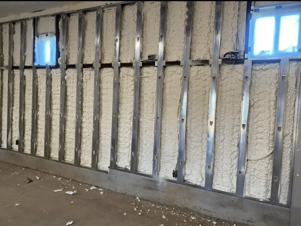 Spray foam insulation filling the cavities between metal studs on a wall above a concrete floor