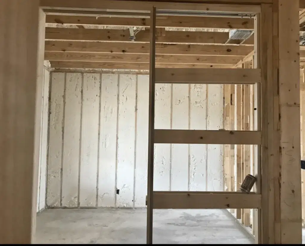 Spray foam insulation between wood studs in a framed room with exposed ceiling joists